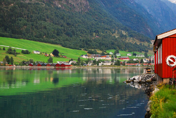 Traditional wooden red cottages on the shores of a fjord in Norway. In the background mountains and houses in a small village. Norwegian landscape.