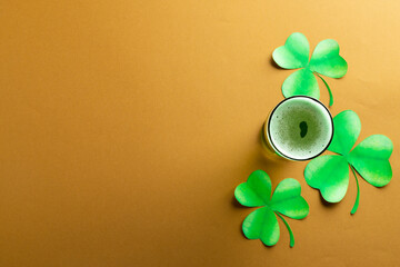 Image of glass with green beer, clover and copy space on orange background © vectorfusionart