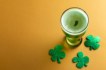 Image of glass with green beer, clover and copy space on orange background © vectorfusionart