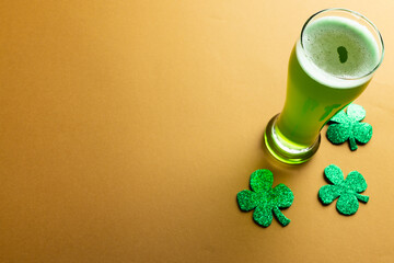 Image of glass with green beer, clover and copy space on orange background © vectorfusionart