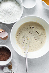 Foamy Eggs and brown sugar that has been whisked together in a white mixing bowl, baking process for making pastries
