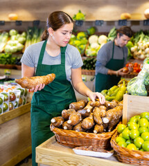 Positive saleswoman in apron offering cassava root on the supermarket