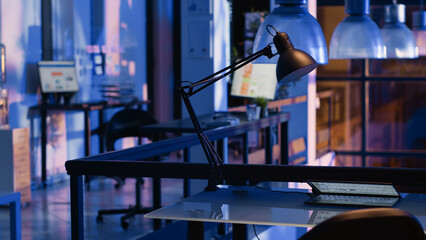 Interior of empty startup office with furniture at night time, having financial graphics report showing on computer monitor. Marketing company desk with nobody in it, place of business.