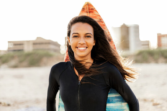 Portrait of a beautiful young female surfer posing with her surfboard at the beach