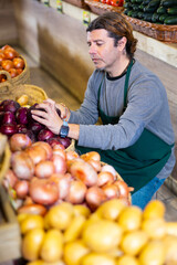 Male grocery store worker arranges red onion and other vegetables on the counter and display case