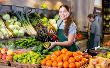 Fototapeta Saleswoman near fruit and vegetables stalls offering to buy green bell peppers obraz