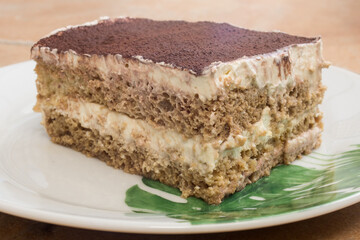 A CLOSE-UP OF A Homemade Sugar-Free Tiramisu on a White Plate with Green Floral Decor. Healthy Dessert with Cream, soft cheese, Cocoa, and Coffee Layers. Ceramic Countertop Split Shot.