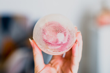 Female hand holding a frozen sphere with a rose inside, soft blurred background.