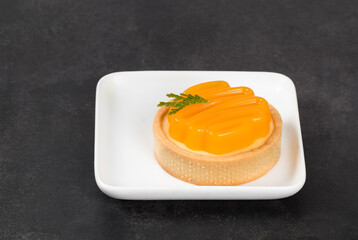 Round tartlet with custard tangerine cream and curly tangerine jelly on top. Dark  grey background