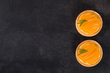 Round tartlet with custard tangerine cream and curly tangerine jelly on top. Dark  grey background. Top view. Copy space