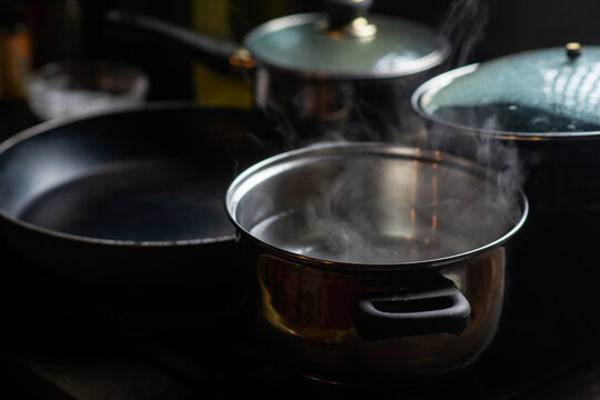 A pot of boiling water on a kitchen stove. Kitchen utensils are nearby.