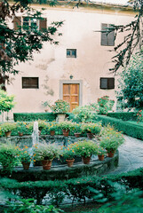 Fountain near an old villa surrounded by blooming flower pots