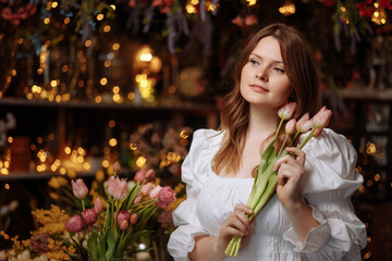 A young woman in white clothes is holding and smelling the smell of a bouquet of flowers. The girl inhales the scent of pink tulips, a gift for International Women's Day or Valentine's Day.