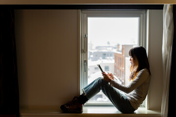Asian woman freelance sitting by the window in bedroom working on digital tablet or study online...