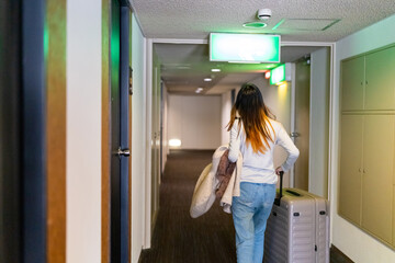 Fototapeta na wymiar Asian woman walking down hotel corridor with suitcase to her room. Businesswoman working outside office. Attractive girl traveler enjoy travel on holiday vacation. Hotel and resort business concept.