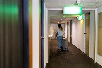 Asian woman walking down hotel corridor with suitcase to her room. Businesswoman working outside office. Attractive girl traveler enjoy travel on holiday vacation. Hotel and resort business concept.