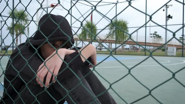 Teen immigrant by school fence. An upset teen girl sits by school playground fence in the open air.