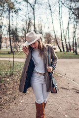 Beautiful woman wearing stylish blazer hat and boots in park. Spring female fashionable outfit in white and brown color.