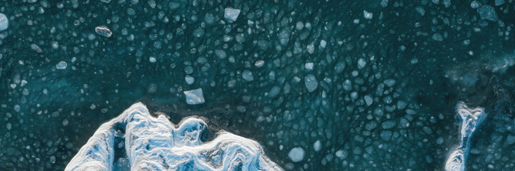 Top view of the freezing sea. Winter aerial photograph of the icy coast and ice floes in sea water. Nature of the Extreme North. Cold frosty winter weather. Harsh arctic climate. Natural background. © Andrei Stepanov