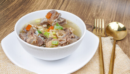 Sop Iga (Beef ribs soup) is Indonesian soup. served in white bowl. selective focus
