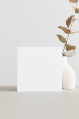 Square invitation card mockup with an eucalyptus on the beige table.