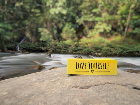Inspirational and Motivational Concept - love yourself text on adhesive note paper. With nature background. Stock photo.