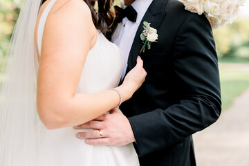 A bride and groom are standing together, her hands are around his suit jacket.