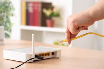 Close up of man hand plugging ethernet cable to router on a desk at home - obrazy, fototapety, plakaty
