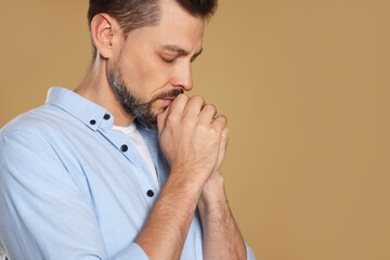 Man with clasped hands praying on beige background, closeup. Space for text