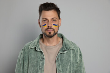Obraz premium Man with drawings of Ukrainian flag on face against light grey background