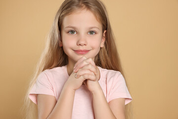 Fototapeta premium Girl with clasped hands praying on beige background