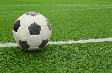 Fototapeta na wymiar Dirty soccer ball on green football field, space for text
