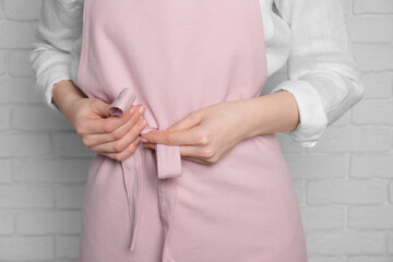 Woman putting on pink apron against white brick wall, closeup
