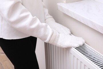 Girl warming hands on heating radiator indoors, closeup