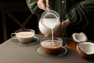 Woman pouring tasty coconut milk into cup of coffee at table, closeup