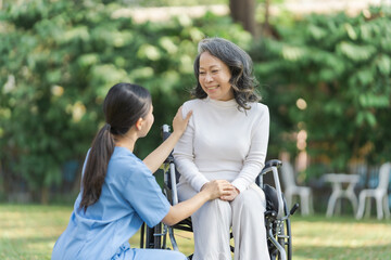 Young asian care helper with asia elderly woman on wheelchair relax together park outdoors to help and encourage and rest your mind with green nature.