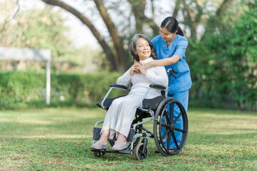 Young asian care helper with asia elderly woman on wheelchair relax together park outdoors to help and encourage and rest your mind with green nature. Hugging