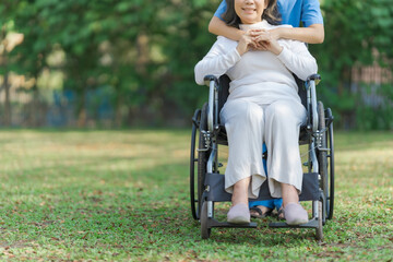 Young asian care helper with asia elderly woman on wheelchair relax together park outdoors to help and encourage and rest your mind with green nature. Hugging