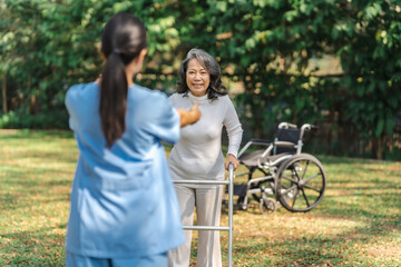 Young asian care helper with asia elderly woman on wheelchair relax together park outdoors to help and encourage and rest your mind with green nature. Help support yourself to learn to walk. walker