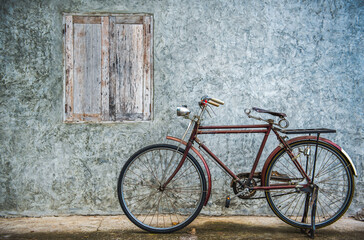 Vintage bicycle on old rustic dirty wall house, many stain on wood wall. Classic bike old bicycle on decay brick wall retro style. Cement loft partition and window background.