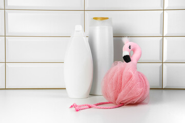 Shower gel,  towel and soft bath, body sponge and shampoo in the bath on a white tile. Composition with body care accessories and beauty products. Flamingo Body Sponge. Morning routine