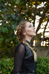Close up portrait of beautiful female model with blonde plait, wearing black leather catsuit,...