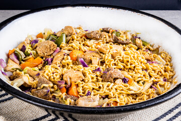 Japanese yakisoba with stir-fried noodles in metallic white pan on table with white tablecloth and black background