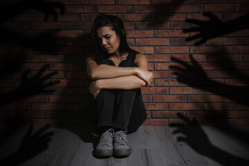 Paranoid individual. Scared woman sitting near brick wall and having delusion as hands reaching for...