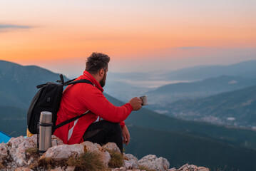 A male hiker relaxing while drinking a cup of coffee during the hiking on the mountain adventure...