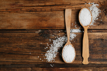 Obraz na płótnie Canvas Spoons with natural sea salt on wooden table, flat lay. Space for text