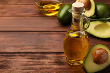 Glass bottle of cooking oil and fresh avocados on wooden table, closeup. Space for text