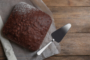 Homemade chocolate sponge cake and spatula on wooden table, flat lay. Space for text