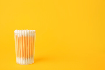 Container with new cotton buds on yellow background. Space for text