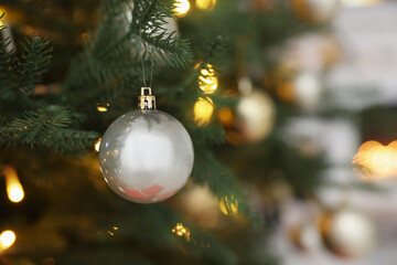 Beautiful silver Christmas ball hanging on fir tree branch against blurred background, closeup. Space for text